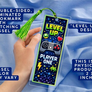 May include: Double-sided, laminated bookmark with a green tassel. The bookmark features a "Level Up" design with a game controller, heart, and pixelated graphics. The text "Player One" is also visible. The bookmark measures 2 x 6 inches.