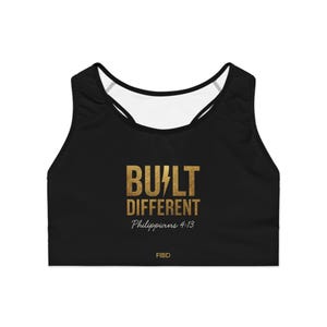May include: Black sports bra with a white racerback design. The front features the gold text "BUILT DIFFERENT" with a lightning bolt graphic, the scripture "Philippians 4:13", and the brand name "FIBD".