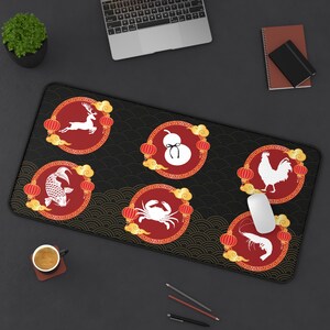 Puede incluir: Alfombrilla de escritorio rectangular negra con seis diseños circulares rojos. Cada diseño presenta una ilustración blanca de un ciervo, una calabaza, un pez, un cangrejo, un gallo y un camarón, enmarcados con nubes doradas y linternas. La alfombrilla tiene un patrón de olas negras.