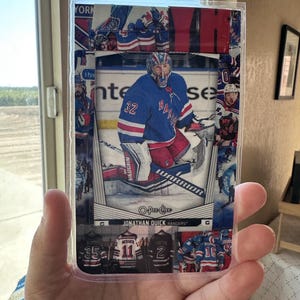 May include: A hockey trading card featuring Jonathan Quick of the New York Rangers in a blue jersey with the number 32. The card has a white border and includes the text "O-Pee-Chee" and "Rangers".