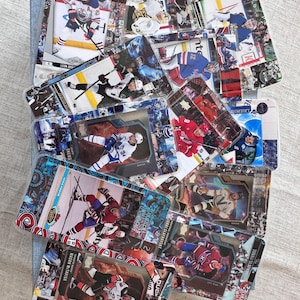 May include: A collection of hockey trading cards featuring various players in action. The cards display team logos and player names, with a mix of action shots and posed portraits. The cards are arranged on a light-colored surface.