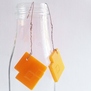 May include: A pair of yellow geometric earrings with a wire design. The earrings are hanging from a glass jar.