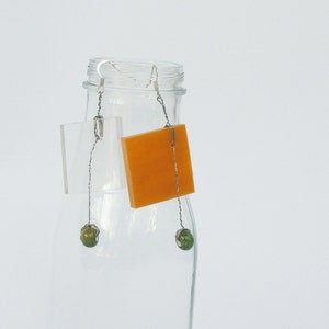 May include: A pair of earrings with orange square-shaped charms and green beads hanging from silver hooks.