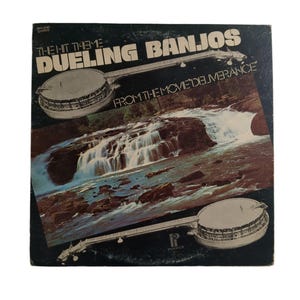May include: Vintage vinyl record album cover for "Dueling Banjos" from the movie "Deliverance." The cover features two banjos and a waterfall scene. The album title is in large white letters, with the movie title below.
