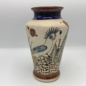 May include: Hand-painted ceramic vase with a cream-colored speckled finish. The vase features a bird design with blue, green, and brown accents. The rim is dark blue and brown. A decorative piece for the home.