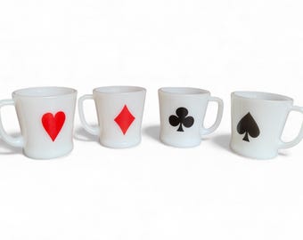 May include: Four white ceramic mugs with playing card suit symbols: a red heart, a red diamond, a black club, and a black spade. Each mug has a handle and a slightly angled design, perfect for a card game enthusiast.
