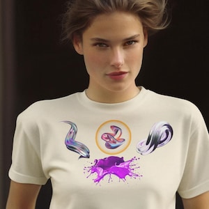 Puede incluir: Una camiseta color crema con un diseño gráfico con formas abstractas en morado, plateado y negro, junto con una salpicadura de pintura morada. La camiseta tiene cuello redondo y mangas cortas.