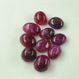 Puede incluir: Una colección de piedras preciosas pulidas, de forma ovalada, en varios tonos de rojo y púrpura. Las piedras preciosas tienen una superficie lisa y brillante y están dispuestas sobre un fondo blanco. Estas piedras preciosas podrían usarse para la fabricación de joyas.