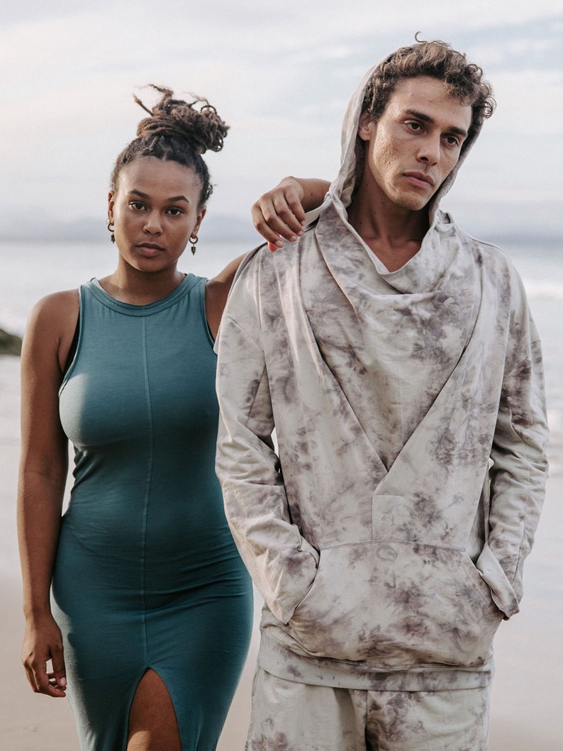 Peut inclure: Un homme et une femme debout sur une plage. L'homme porte un sweat &agrave; capuche gris clair avec un motif tie-dye. La femme porte une robe sans manches turquoise.