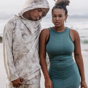 Peut inclure: Un homme et une femme debout sur une plage. L'homme porte un sweat &agrave; capuche gris clair avec un motif tie-dye. La femme porte une robe sans manches turquoise.