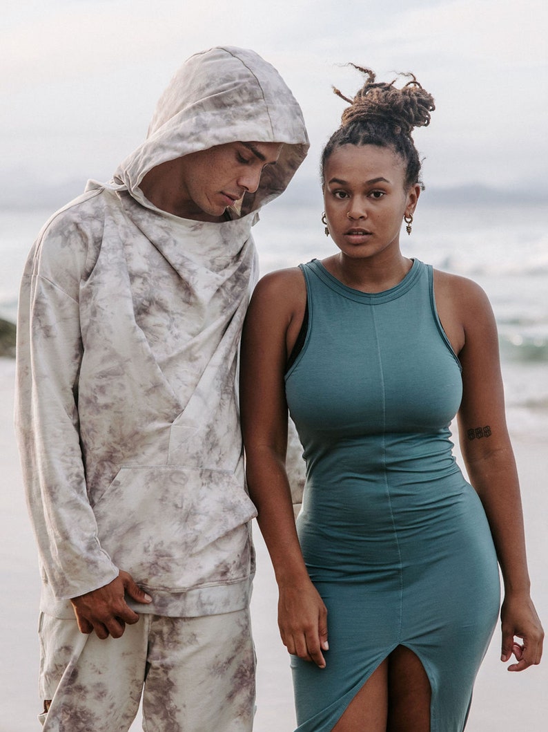Peut inclure: Un homme et une femme debout sur une plage. L'homme porte un sweat &agrave; capuche gris clair avec un motif tie-dye. La femme porte une robe sans manches turquoise.