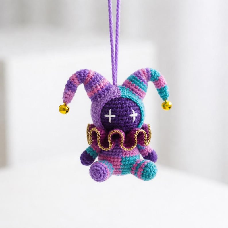 May include: A handmade crochet jester doll in purple, teal, and pink. The doll has a jester hat with bells, a gold collar, and cross-shaped eyes. It is suspended by a purple string.