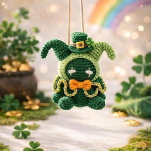 May include: A handmade green crochet leprechaun doll with a small hat and orange bow tie. The doll is suspended by a string against a backdrop of a rainbow, shamrocks, and gold coins, evoking a St. Patrick's Day theme.