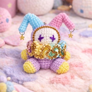 May include: A handmade crochet jester doll in pastel colors. The doll features a purple body, yellow feet, a ruffled collar, and a blue and pink hat. Gold star charms dangle from the hat. The doll is surrounded by other crochet items.