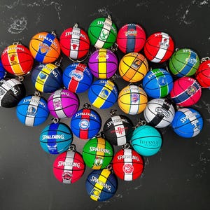 Könnte beinhalten: Eine Sammlung von Miniatur-Basketball-Schlüsselanhängern, die jeweils ein anderes Teamlogo und Farbschema aufweisen. Die Schlüsselanhänger sind rund, mit dem Wort "SPALDING" aufgedruckt. Die Schlüsselanhänger sind in verschiedenen Farben erhältlich, darunter Rot, Blau, Grün und Gelb.