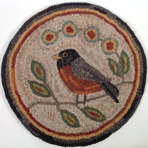 Puede incluir: Alfombra redonda, hecha a mano, con un dise&ntilde;o de p&aacute;jaro. La alfombra muestra un petirrojo con la espalda gris, el pecho naranja y la cabeza negra, posado en una rama con hojas verdes. El borde incluye tonos marrones, rojos y negros, creando una est&eacute;tica r&uacute;stica.