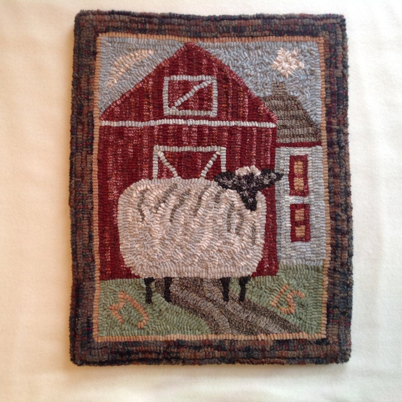 May include: A handcrafted, rectangular rug featuring a barn scene with a sheep. The barn is red with a white door and window. The sheep is white with a black face, standing on green grass. The rug has a brown border.