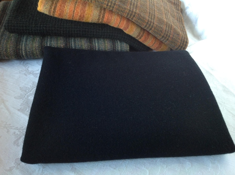 Peut inclure: Un morceau de tissu noir et rectangulaire, peut-&ecirc;tre de laine ou de feutre, est au centre de l'image. Plusieurs textiles pli&eacute;s dans les tons de marron, d'orange et de vert sont empil&eacute;s derri&egrave;re. Les tissus pr&eacute;sentent divers motifs, notamment des rayures et des textures tiss&eacute;es.