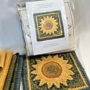 May include: A rug hooking kit featuring a sunflower design. The kit includes a finished 8" x 8" rug, materials, and instructions. The sunflower has yellow and brown petals with a green and blue border. The packaging includes the text "Designs In Wood / Mary Johnson".
