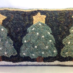May include: A rectangular decorative pillow featuring three Christmas trees with star toppers. The trees are green with white accents, set against a dark background. The pillow has a light-colored border and measures approximately 12 inches long.
