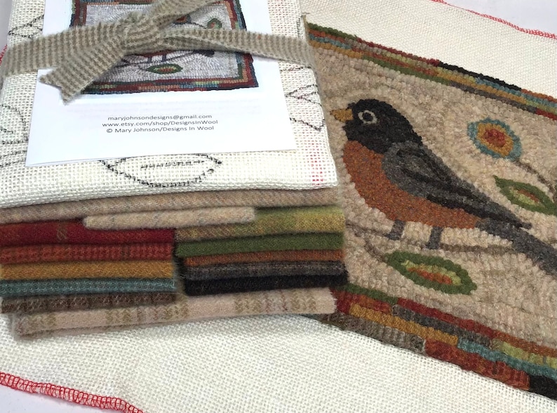May include: A stack of wool fabric squares in various colors, with a finished rug featuring a bird design. The rug is beige with a colorful border and a detailed image of a bird. A printed paper with text is tied with a beige ribbon.