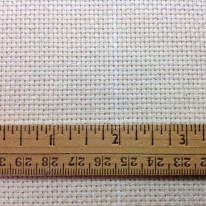 Peut inclure: Gros plan sur un tissu beige pour point de croix avec une r&egrave;gle en bois. La r&egrave;gle est gradu&eacute;e en pouces, affichant des mesures jusqu'&agrave; 7,6 cm. Le tissu pr&eacute;sente un motif quadrill&eacute;, id&eacute;al pour les travaux d'aiguille.