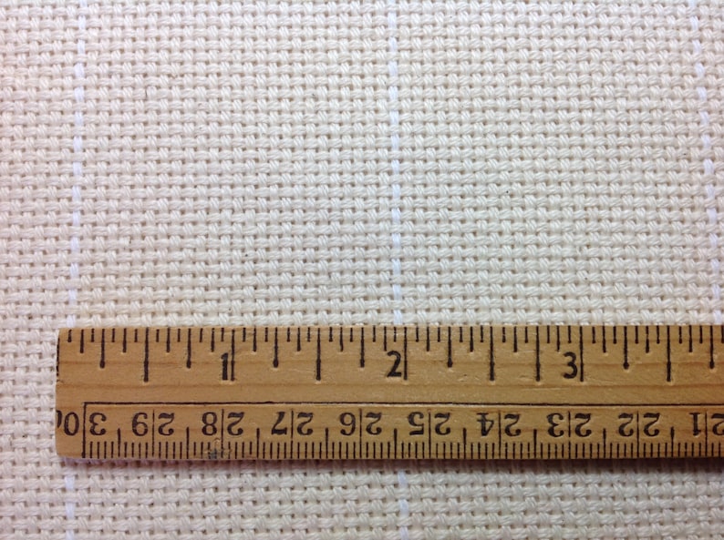 Peut inclure: Gros plan sur un tissu beige pour point de croix avec une r&egrave;gle en bois. La r&egrave;gle est gradu&eacute;e en pouces, affichant des mesures jusqu'&agrave; 7,6 cm. Le tissu pr&eacute;sente un motif quadrill&eacute;, id&eacute;al pour les travaux d'aiguille.