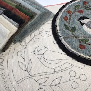 May include: A collection of fabric swatches in various colors, including gray, green, and black, alongside a completed round rug with a bird design. The rug features a black border and a light blue background with floral accents. A canvas with a bird outline is also visible.