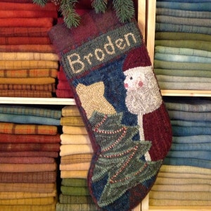 May include: A handmade Christmas stocking with the name "Broden" embroidered on it. The stocking features a Santa Claus design, a Christmas tree, and a bear. The stocking is red, blue, green, and beige.