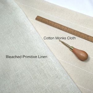 May include: An overhead shot shows two types of fabric: Bleached Primitive Linen and Cotton Monks Cloth. A wooden ruler with inch markings and a wooden-handled needle tool are also present. The fabrics are off-white and beige.