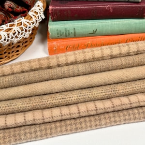 May include: A stack of tan and brown fabric rolls with various patterns, including checks and stripes. A wicker basket with a white lace trim and a stack of vintage books are in the background.