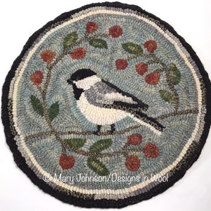 May include: A round, hand-hooked rug featuring a bird perched on a branch with berries. The bird has a black head and white body, set against a blue background. The rug has a black border and the text "Mary Johnson/Designs in Wool".