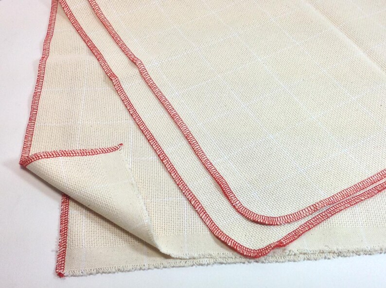 Peut inclure: Tissu blanc cass&eacute; avec un motif quadrill&eacute; et des coutures rouges sur les bords. Le tissu est pli&eacute;, r&eacute;v&eacute;lant la texture et la construction du mat&eacute;riau. Les coutures rouges offrent un d&eacute;tail contrastant.