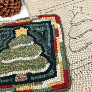 May include: A handcrafted Christmas tree rug with a star on top, featuring green, white, and blue hues. The rug is bordered with red, yellow, and green. Two pine cones are in the background, along with a burlap Christmas tree outline.