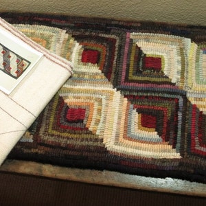 May include: Handmade rug with a geometric pattern featuring squares in shades of red, brown, green, and beige. The rug is made of woven fabric and has a cream-colored backing. A diagram of the rug's design is visible.