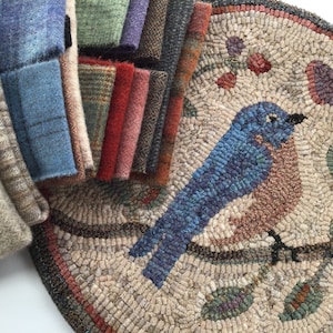 Puede incluir: Una pila de muestras de tela de lana de varios colores junto a una alfombra redonda con un dise&ntilde;o de p&aacute;jaro azul. La alfombra presenta un p&aacute;jaro detallado posado en una rama con hojas y bayas. Las muestras de tela incluyen tonos de azul, verde, rojo y marr&oacute;n.