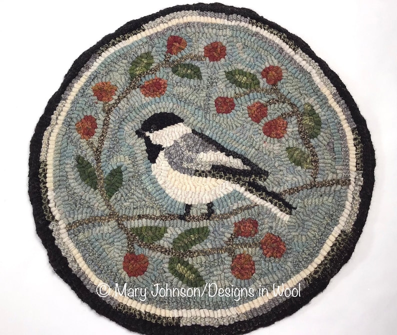 May include: Round, hand-hooked rug featuring a bird perched on a branch with berries. The rug has a light blue background with a black border. The bird is black, white, and gray. The rug measures approximately 24 inches in diameter.