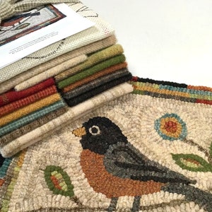 May include: A handcrafted rug with a detailed bird design, featuring a black-headed robin with an orange breast, perched on a branch with a flower. A stack of fabric squares in various colors is tied with a ribbon, complementing the rug's color palette.
