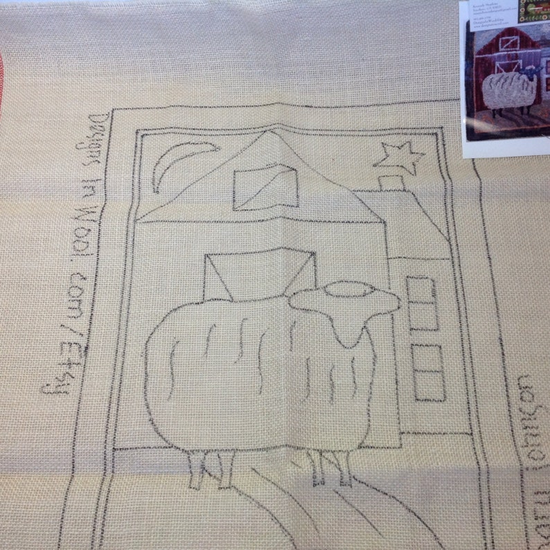 May include: A beige rug hooking pattern featuring a sheep in front of a barn, with a moon and star in the sky. The design is outlined in black ink. Text on the left side reads "designs in wool.com/etsy".