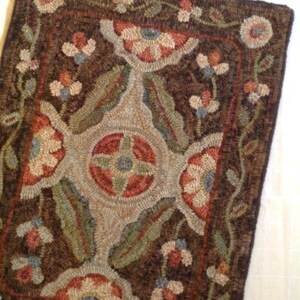 Puede incluir: Una alfombra rectangular hecha a mano con un dise&ntilde;o floral. La alfombra presenta un fondo marr&oacute;n oscuro con un medall&oacute;n central y motivos florales en las esquinas en tonos de rojo, verde, azul y crema. El borde de la alfombra tambi&eacute;n es marr&oacute;n oscuro.