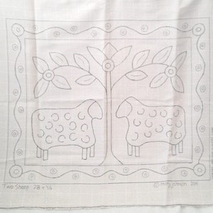 K&ouml;nnte beinhalten: Beige Stoffpaneel mit handgezeichnetem Design von zwei Schafen und einem Baum mit Blumen, umrahmt von einem dekorativen Rand. Der Text "Two Sheep 71 x 91 cm" befindet sich unten, mit der Signatur des K&uuml;nstlers.