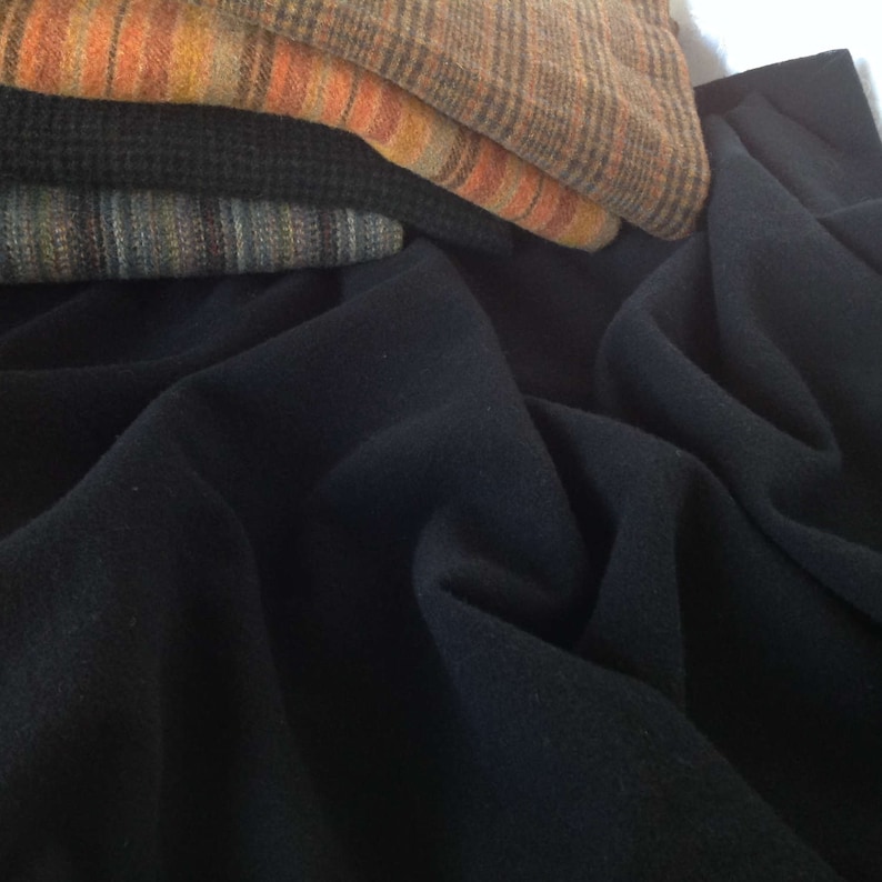 Peut inclure: Un empilement de tissus pli&eacute;s de diff&eacute;rentes couleurs et motifs. La couche sup&eacute;rieure est un plaid marron et orange, suivi d'un tissu textur&eacute; bleu fonc&eacute; et d'un tissu ray&eacute;. Un grand morceau de tissu bleu fonc&eacute; est drap&eacute; en dessous.