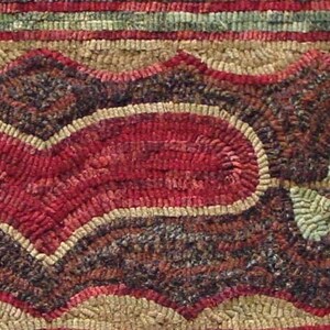 May include: Close-up of a handmade rug with a heart and rose design. The heart is red with a tan border, and the rose is red with green leaves. The background is a mix of brown, tan, and green.