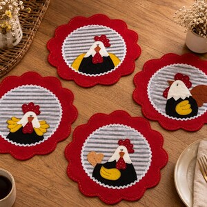 Puede incluir: Cuatro posavasos redondos de tela con bordes rojos festoneados y un círculo central de rayas grises y blancas. Cada posavasos presenta una aplicación de tela de un gallo con cabeza blanca, cresta roja, cuerpo negro y alas amarillas.