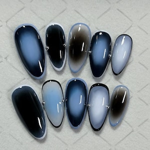May include: Set of ten oval-shaped artificial nails. Each nail features a gradient design in shades of blue, black, and white, with a glossy finish. A small silver accent is placed on each nail.