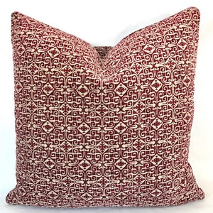 May include: A red and white patterned throw pillow with a geometric design. The pillow is made of a soft, woven fabric.
