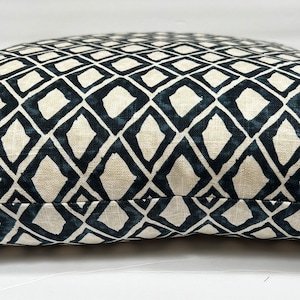 May include: A close-up of a cream-colored pillow with a black and white geometric diamond pattern. The pillow is made of a soft, textured fabric.