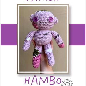May include: A handmade crochet doll in shades of lavender and pink, with stitched details and button eyes. The doll has a patchwork design, with the word "HAMBO" below and "PATRON" above.