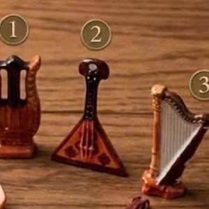 May include: Miniature musical instruments, including a lyre, a balalaika, and a harp, are displayed on a wooden surface. The instruments are primarily brown with black and white accents. Each instrument has a unique shape and design, showcasing detailed craftsmanship.