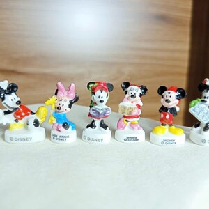 Puede incluir: Colecci&oacute;n de siete figuras de personajes de Disney, incluyendo Mickey Mouse, Minnie Mouse y Donald Duck. Cada figura est&aacute; sobre una base blanca con la palabra "Disney". Las figuras son de colores brillantes y miden unos 5 cm de altura.